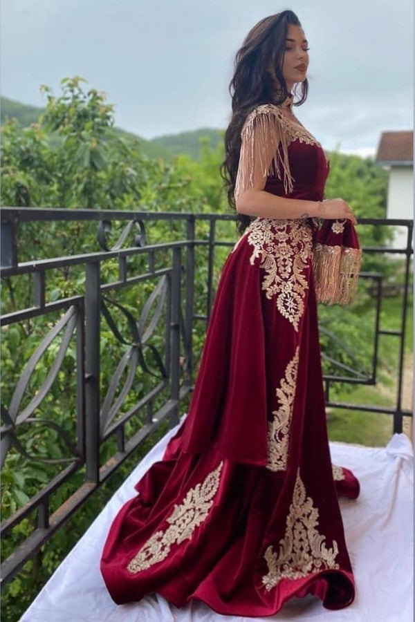 Vestido de noche largo rojo vino con apliques florales dorados de terciopelo y abertura.